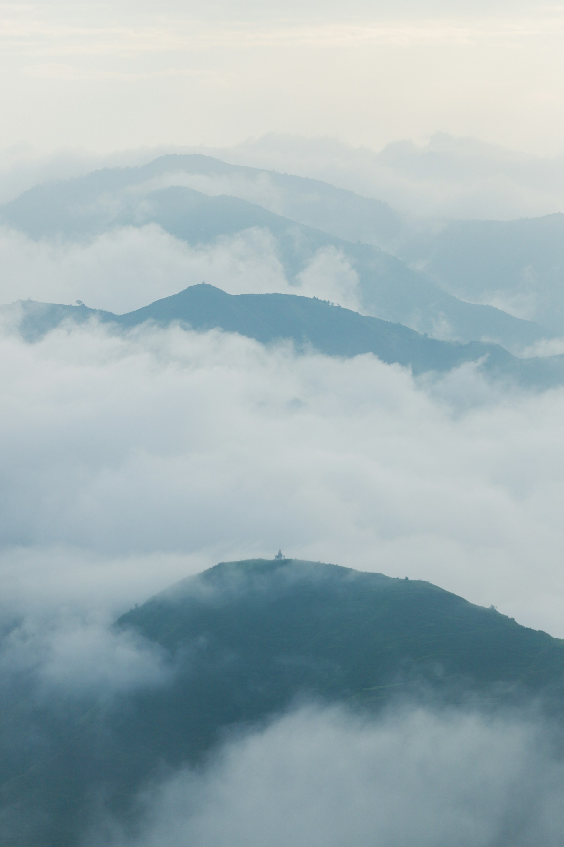 Misty mountains shrouded in soft clouds at dawn.